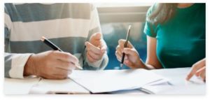 A boy and a girl sitting together, focused on filling out forms with pens in hand