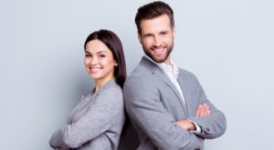 A man and a woman both smiling while wearing gray business suits, presenting a professional and friendly appearance