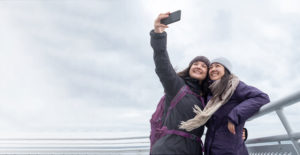 Two girls taking a selfie with a beautiful backdrop of fluffy clouds in the sky