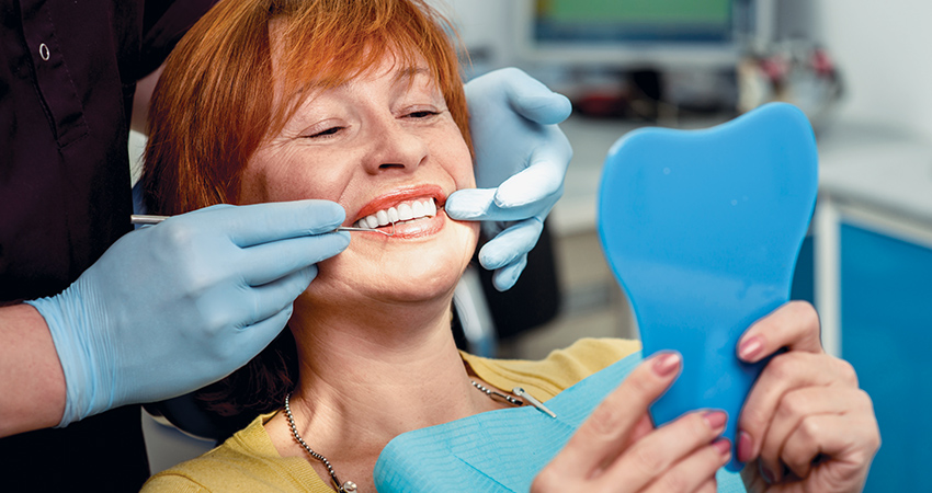 a woman in the dentist chair looking into a mirror and smiling widely